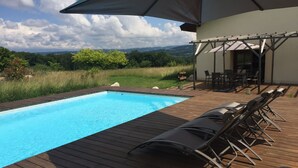 Une terrasse en bois avec une piscine, des chaises longues et une pergola équipée d’une table et de chaises.