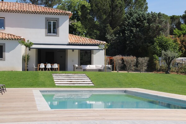 Une maison moderne dotée d’une piscine, d’un patio avec mobilier d’extérieur et d’une pelouse bien entretenue.