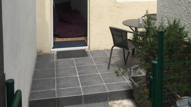 A small patio area with a tiled floor, a single table and chair, and a door leading to an interior space.