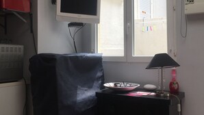 A room with a desk, a computer, a television, and a window with blinds.