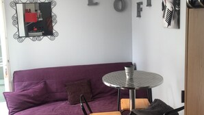 A room with a purple sofa, a small round table with a cup, and a mirror with decorative frames.