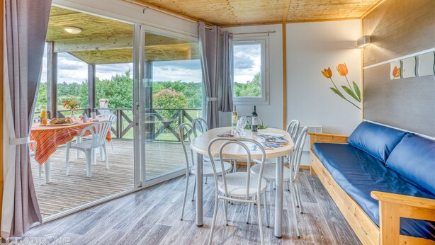 Une pièce avec un plafond en bois, une table à manger avec des chaises, un canapé bleu et une grande fenêtre donnant sur un paysage verdoyant.