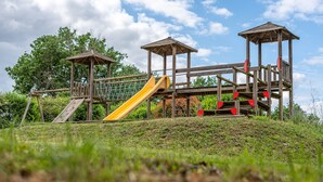 Une aire de jeux en bois, dotée de toboggans et de structures d’escalade, entourée de verdure.
