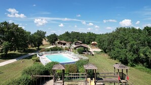 Un espace piscine doté d’une terrasse entourée d’une clôture, de petits kiosques en bois et offrant une vue dégagée sur le paysage environnant.