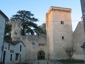 A historic stone building with a central tower, a courtyard, and a tree in the background.
