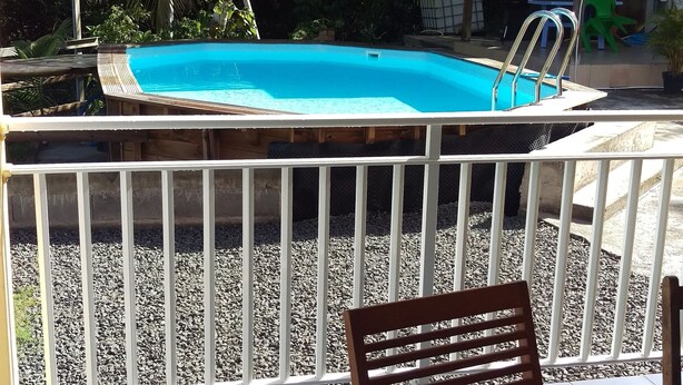 Una piscina con cerca blanca, rodeada de palmeras y un patio con mesa y sillas.