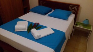 Una cama bien hecha con ropa de cama azul y blanca, dos toallas blancas enrolladas y un arreglo floral decorativo.