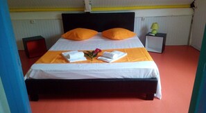 Una cama bien hecha con ropa de cama blanca y naranja, dos almohadas y un pequeño arreglo floral.