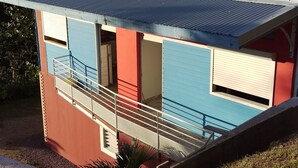 Un edificio de dos pisos con techo de lámina corrugada, antena parabólica y balcón.