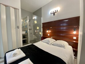 Une chambre d’hôtel comprenant un lit, une tête de lit en bois, un espace douche et une armoire.