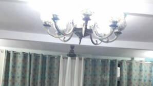 Ein Zimmer mit zwei Sesseln, einem kleinen Tisch, einem gemusterten Vorhang und einer Chandelier.