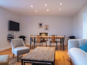 Una sala de estar moderna con una mesa de comedor de madera, sillas, un sofá y un televisor montado en la pared.