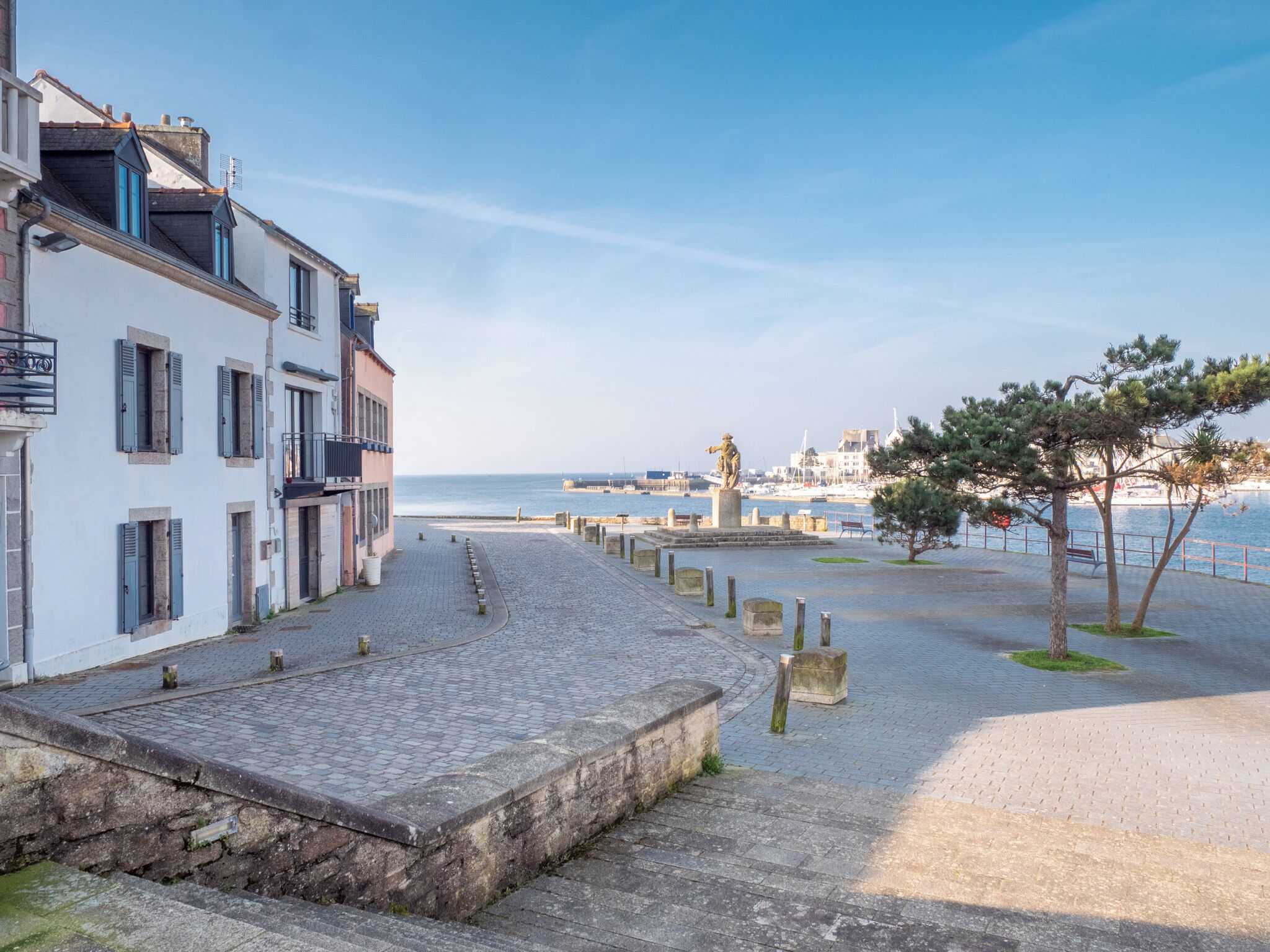 A cobblestone pathway leading to a waterfront with buildings and a statue.