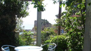 Eine Terrasse im Freien mit einem runden Tisch und vier Stühlen, umgeben von viel Grün und Blick auf die Küste.