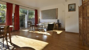 Ein geräumiges Wohnzimmer mit einem großen Schiebeglasfenster, das auf einen Balkon führt, einem karierten Wandbehang und einer Holzdekoration.