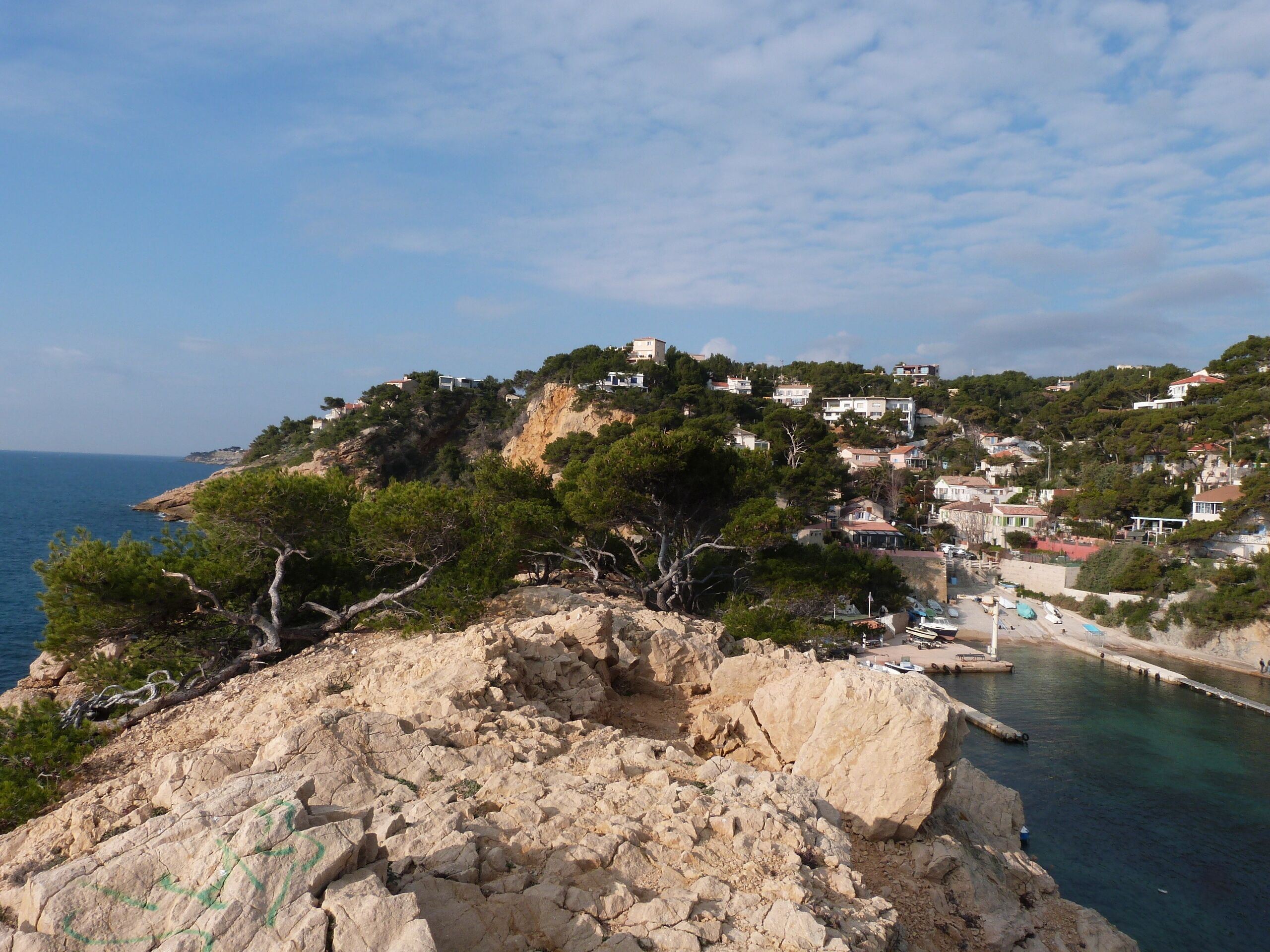 A coastal town with buildings on a hillside, rocky terrain, and a clear view of the sea.