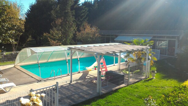 Una piscina techada con tobogán, rodeada por una valla y una zona de estar cubierta.