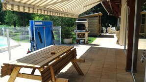 Un área de patio al aire libre con una mesa de madera, un refrigerador azul y un horno para pizza.