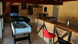 Una habitación con mesa de fútbol, mesa de billar y una zona de bar con una silla roja.