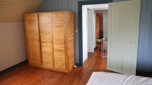 Quarto com guarda-roupa de madeira, uma cama e porta para outro cômodo.