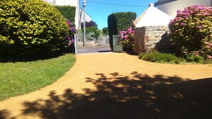 Uma passagem que leva a um portão com muro de pedra e plantas floridas.