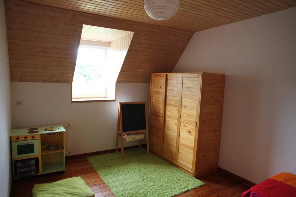 Een kamer met een schuine kap, een houten garderobe, een groen tapijt, een speelkeuken en een raam.