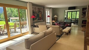 Een ruime woonkamer met een grote schuifpui naar buiten, een zithoek, een salontafel en een schilderij aan de muur.