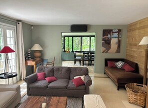 A living room with a grey sofa, a brown sofa, and a wooden coffee table. There is a dining area in the background with a table and chairs.
