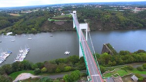 A large suspension bridge spanning a river with boats docked nearby. - Small charming Breton house (Nivillac)