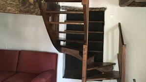 A rustic interior with a wooden spiral staircase, a red sofa, and tiled flooring. - Small charming Breton house (Nivillac)