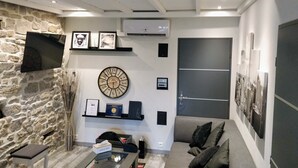 Una sala de estar moderna con una pared de piedra, un reloj redondo, un sofá, una mesa de centro y un televisor de pantalla plana montado en la pared.