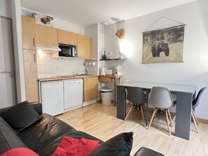 Een compacte leefruimte met kitchenette, een eethoek en een zithoek met bank en stoelen.