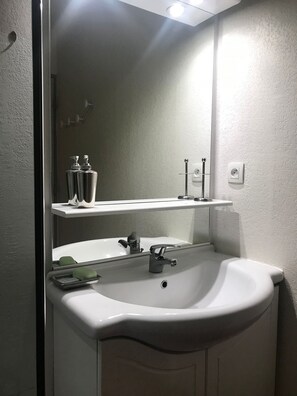 A bathroom with a white sink, a mirror, and a shelf above the sink. - Pied du télécabine. T2 + alcove. Parking couvert. (Cauterets)