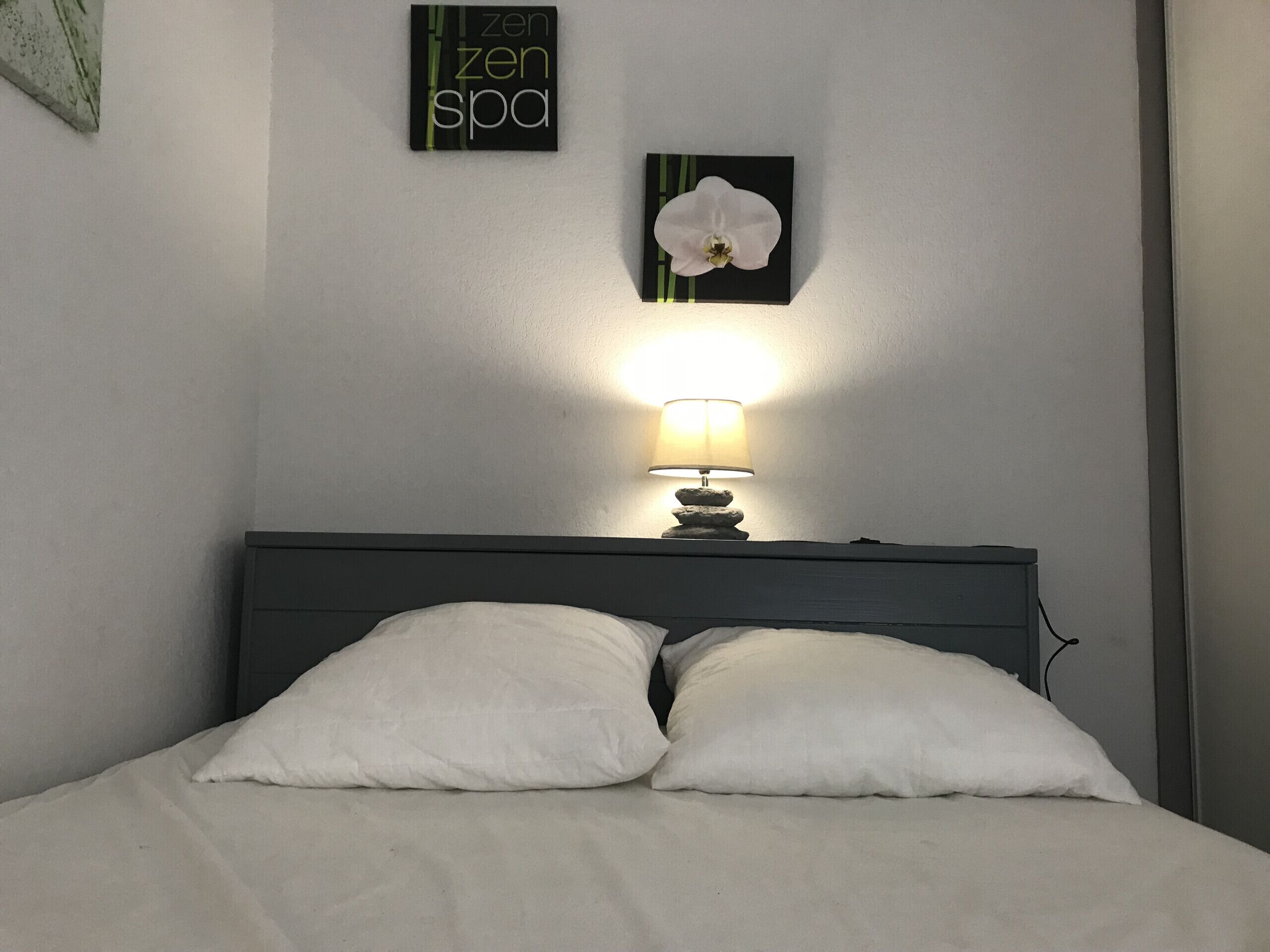 Un lit avec une literie blanche, une table de chevet avec une lampe et deux éléments de décoration murale.