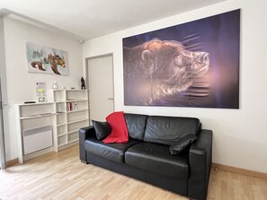 Una sala de estar con un sofá de cuero negro, un cojín rojo, una estantería blanca y un cuadro grande de un oso en la pared.