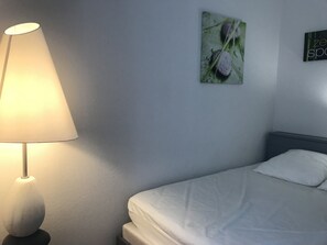 A bed with white bedding, a bedside lamp, and a wall-mounted picture.