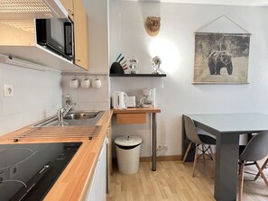 Cocina compacta con microondas, pileta y encimera de madera. Incluye un bote de basura y una pequeña mesa con sillas.