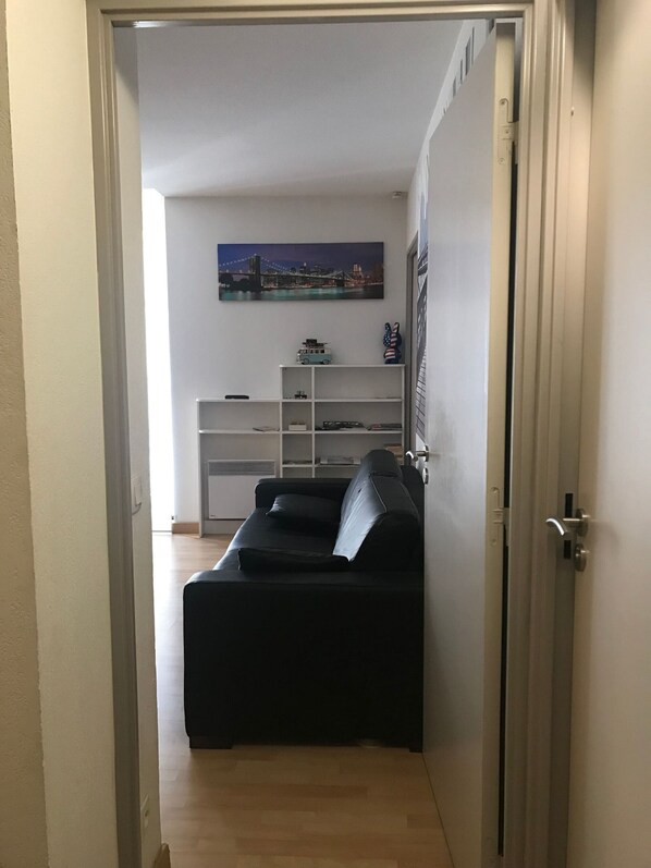 Una sala de estar con un sofá negro, un estante blanco lleno de juguetes y un cuadro de un paisaje urbano en la pared.
