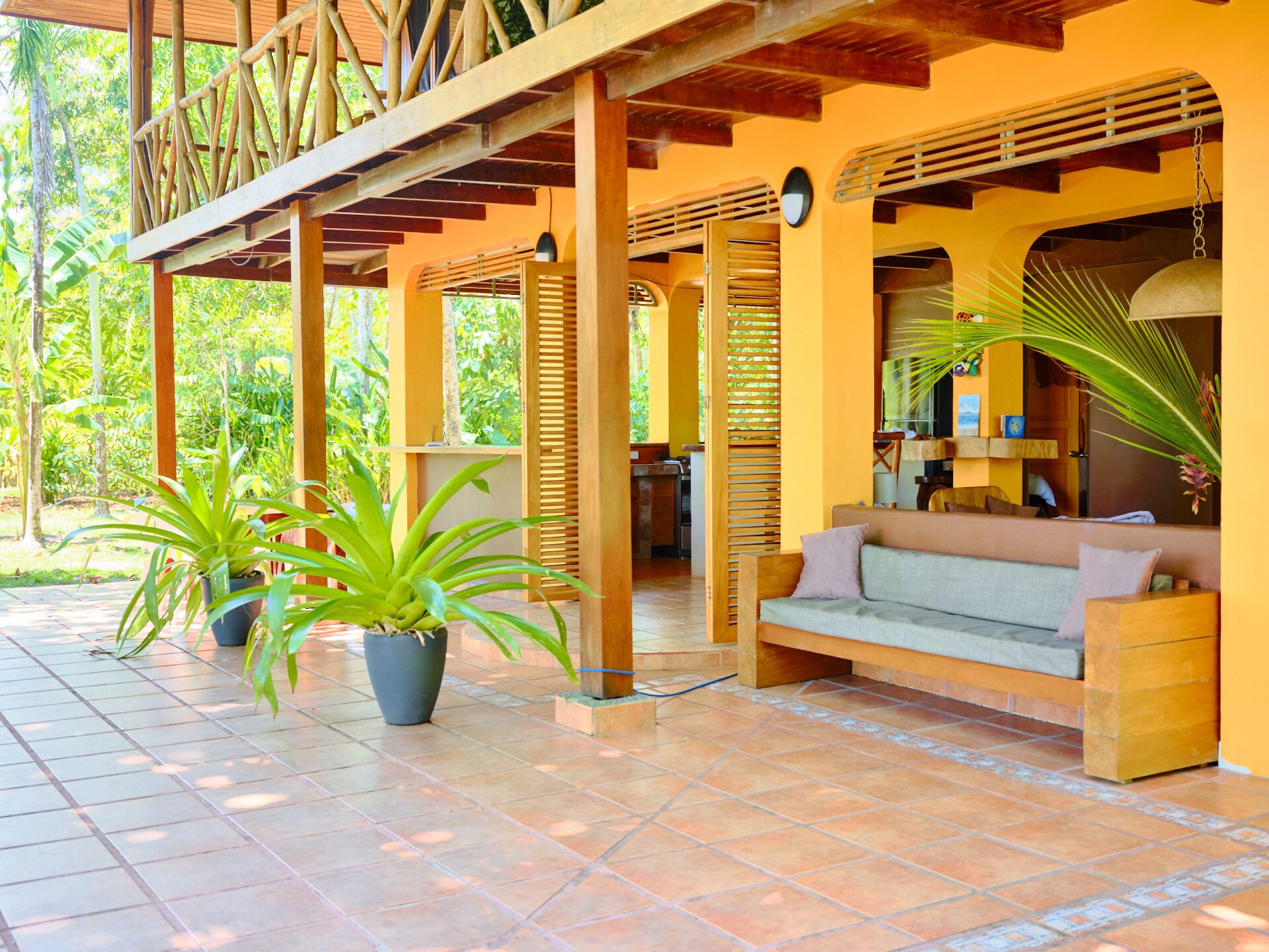 A covered outdoor seating area with a wooden bench and potted plants.