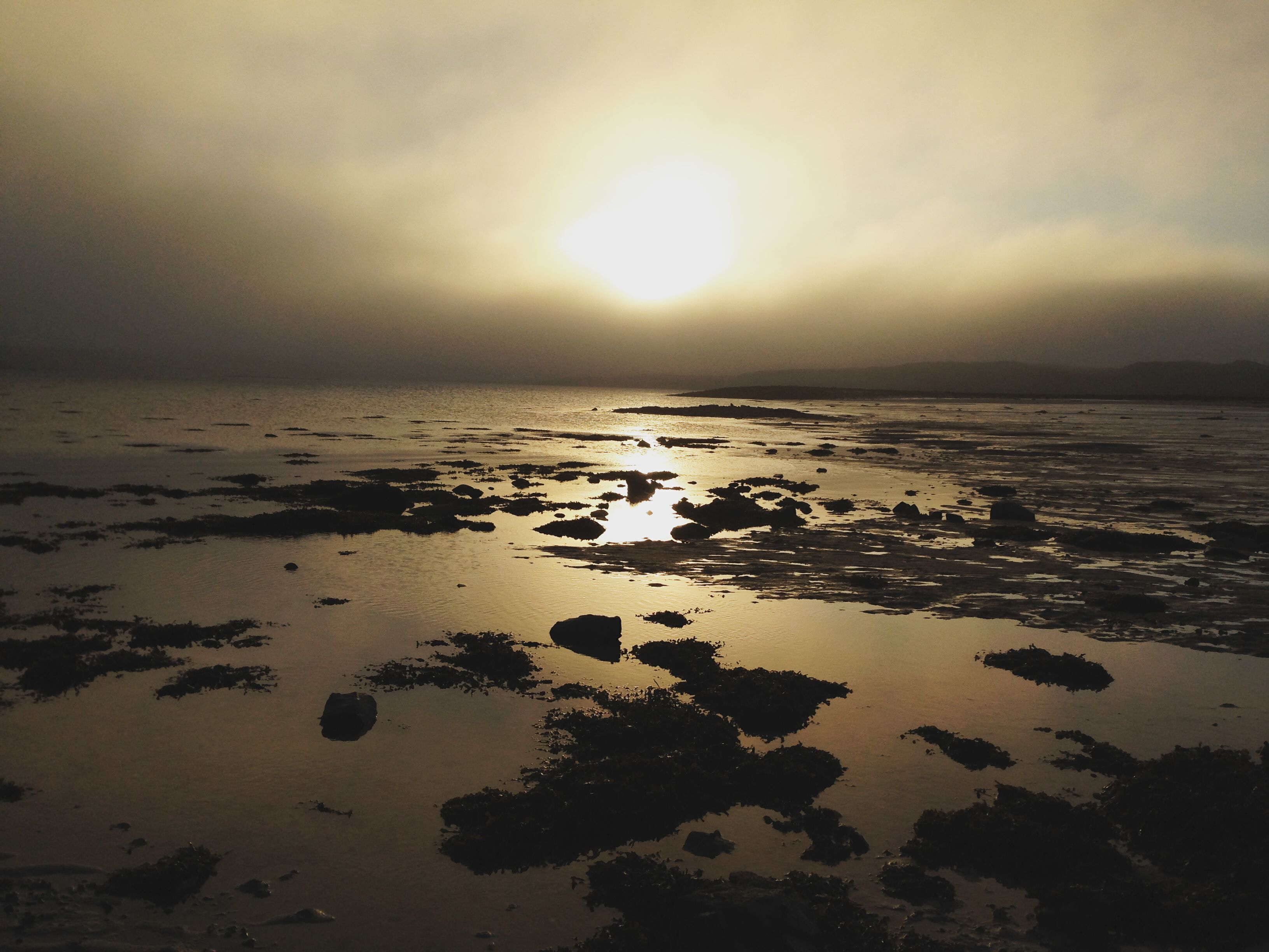 Une plage où le soleil se reflète sur l’eau et les rochers.
