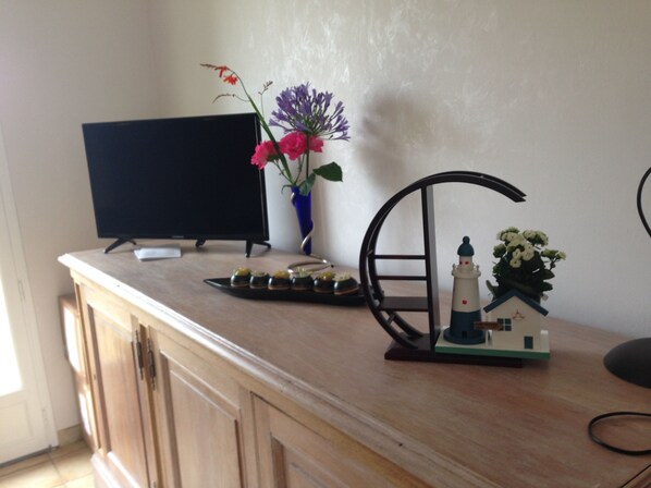 Ein Holztisch mit einem Fernseher, einer Blumenvase, einem Tablett mit Snacks und einem Leuchtturmmodell.