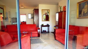 Ein Wohnzimmer mit roten Sofas, einem Couchtisch und einem gemusterten Teppich. An der Wand befindet sich ein Spiegel und eine Kommode mit Dekorationen.