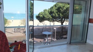 Ein Zimmer mit Glastür und Blick auf einen Strand, ein roter Sessel und ein kleiner Tisch.