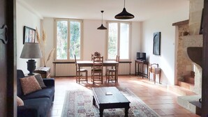 Un salón amplio con sofá, una mesa de centro, una mesa de comedor con sillas, chimenea y ventanas grandes.