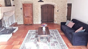 Un salón con alfombra estampada, un sofá oscuro, una mesa de madera con un jarrón y una lámpara colgante.