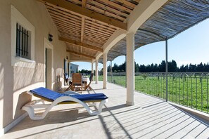 A covered outdoor area with a wooden ceiling, a lounge chair, and a table with chairs.