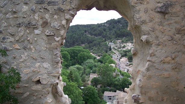 A stone archway leading to a village with buildings and trees. - cccccccccc (Fontaine-De-Vaucluse)