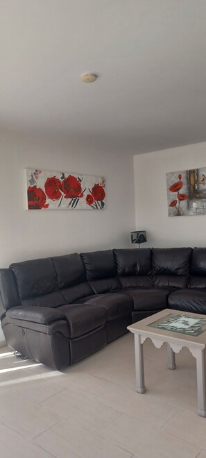 A living room with a black leather sofa, a white coffee table, and two wall-mounted paintings.