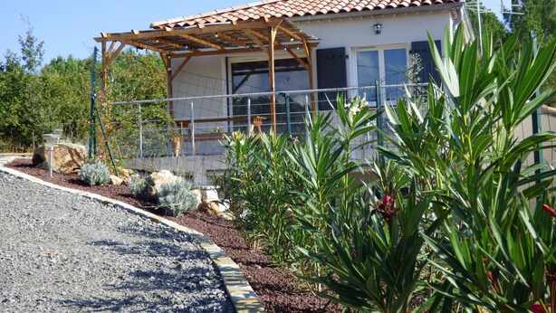 A house with a tiled roof, a covered porch, and a garden with various plants. - Little house with pool 4 people (Payzac)