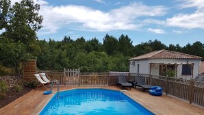 A rectangular swimming pool with a wooden deck, surrounded by a wooden fence. There are lounge chairs and a small building with a tiled roof. - Little house with pool 4 people (Payzac)